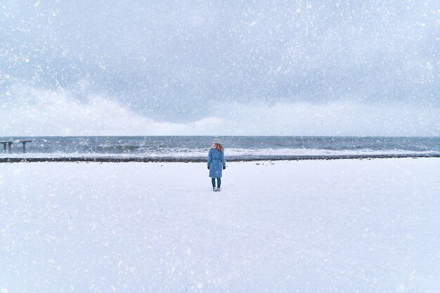 Einsame Frau steht in einem Schneesturm am Schneeufer