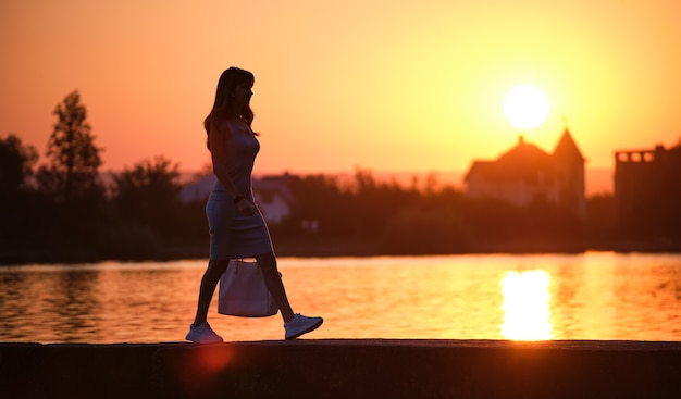 Einsame Fußgängerin, die an einem warmen Abend allein am See spazieren geht. Einsamkeit und Entspannungskonzept.