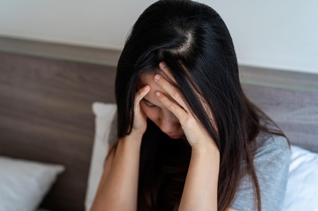 Einsame junge Frau, die sich deprimiert und gestresst fühlt, sitzt im Schlafzimmer Konzept für negative Emotionen und psychische Gesundheit