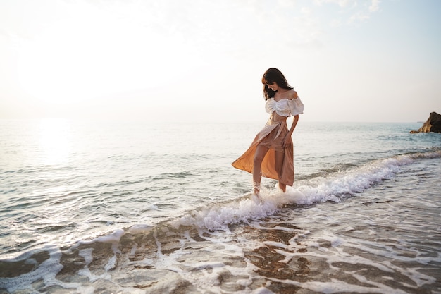 Einsame junge Frau geht bei Sonnenuntergang an der Küste entlang