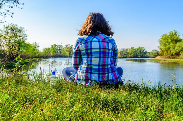 Einsame junge Frau sitzt am Ufer des Flusses