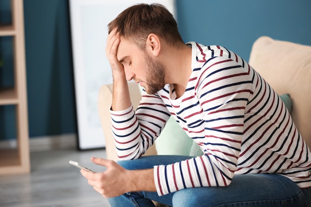 Einsamer depressiver Mann mit Handy zu Hause