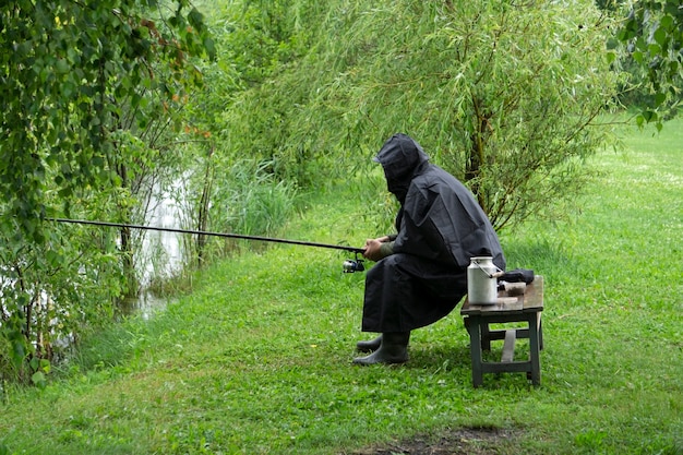 Einsamer Fischer auf einem See bei regnerischem Sommerwetter. Ein Fischer fischt in einem Regenmantel