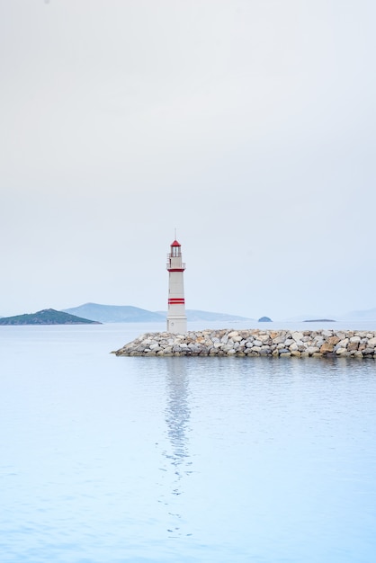 Einsamer Leuchtturm auf einer Steinstraße mitten im Meer mit Ansichten der Berge und des Nebels