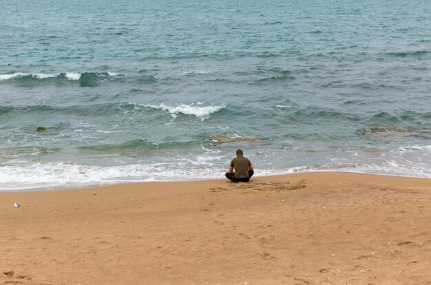 Einsamer Mann sitzt auf dem Sand und blickt auf das Meer