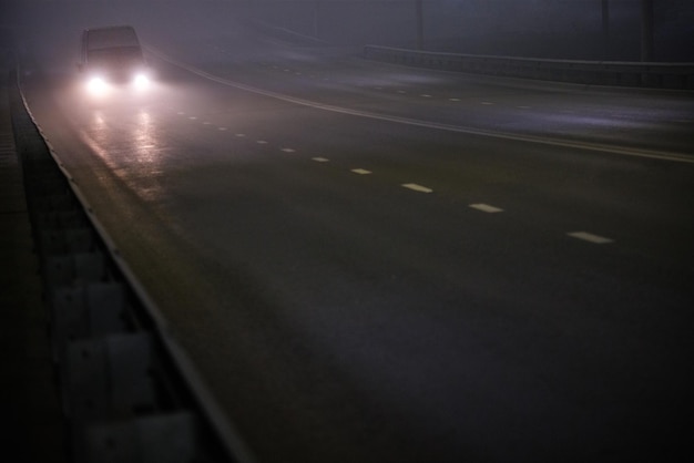 Einsamer Minivan, der sich auf einer leeren, nächtlichen, nebligen Straße bewegt