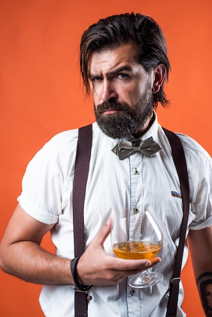 Einsamer Nachtpartygänger mit Alkohol Brandy oder Cognac bärtiger Mann in Hosenträgern trinkt Scotch Whisky brutaler Typ Barkeeper trägt Fliege eleganter männlicher Barmann hübscher Hipster trinkt Rumglas