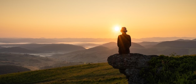 Einsamer Tourist am Rande des Berghügels vor der Kulisse eines unglaublichen Sonnenuntergangs