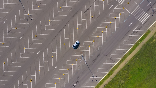 einsames Auto fährt auf dem riesigen leeren Parkplatz mit vielen leeren Parkplätzen