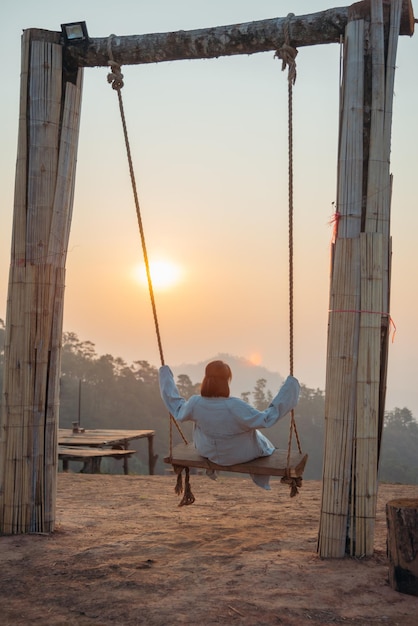 Einsamkeitsfrau, die auf der Schaukel sitzt und bei Sonnenaufgang die Sonne anschaut