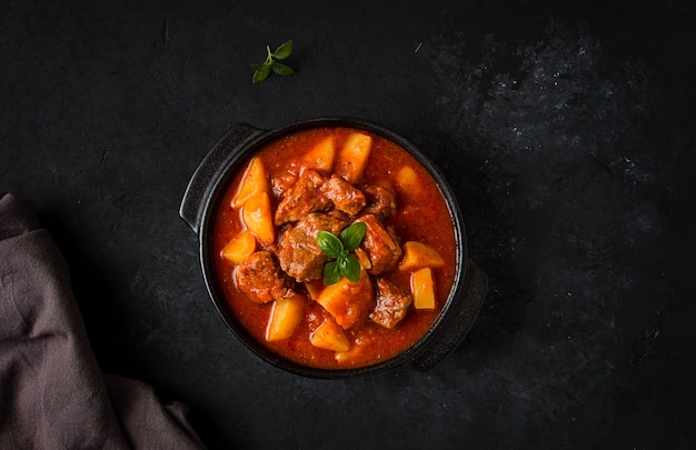 Eintopf mit Kartoffeln in Tomatensauce mit Gewürzen und Kräutern Nahaufnahme keine Menschen auf schwarzem Hintergrund