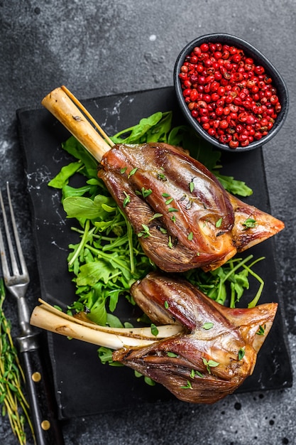 Eintopf Ziegenschenkel auf einem Marmorbrett mit Rucola. Schwarzer Hintergrund. Ansicht von oben.