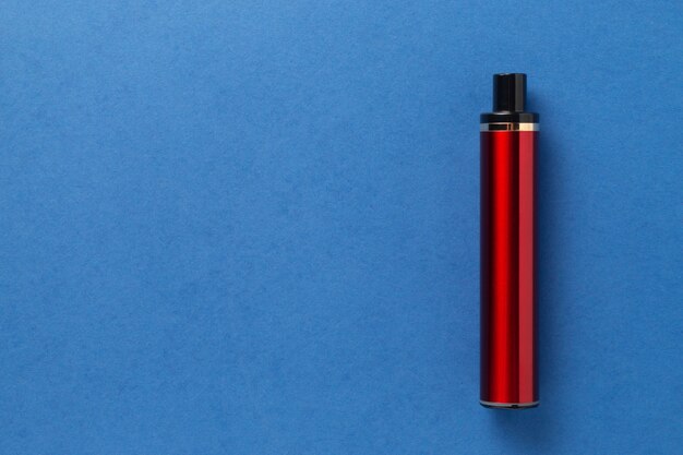 Einweg-E-Zigarette in roter Farbe auf blauem, isoliertem Hintergrund. Das Konzept des modernen Rauchens, Dampfens und Nikotins. Ansicht von oben