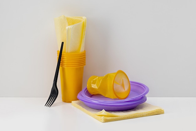 Einwegbecher aus gelbem Plastik und lila Teller, Papierservietten, Gabel.