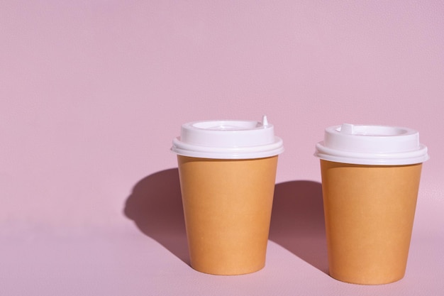 Einwegbecher für heißen Kaffee oder Tee auf rosafarbenem Hintergrund in der hellen Sonne.