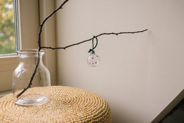 Einzelne Glasweihnachtskugeln auf einem Holzzweig in einer Vase auf hellem Hintergrund und einem Fenster. DIY Neujahr und Weihnachten kreative Raumdekorationsidee. Minimales skandinavisches Ornament.