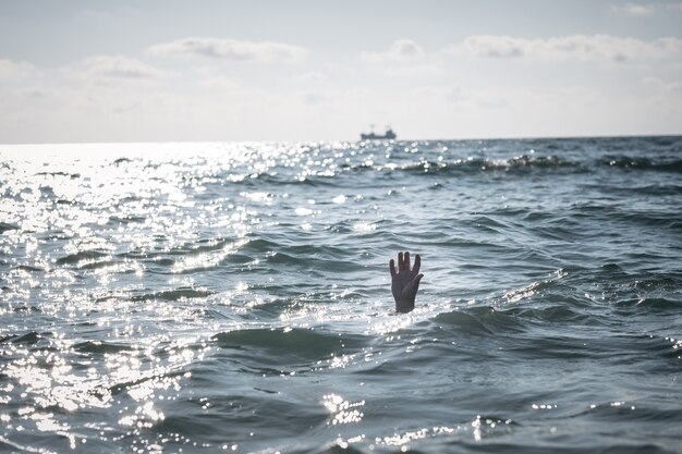 Einzelne Hand des Ertrinkenden im Meer, der um Hilfe bittet. aus dem Wasser ragen