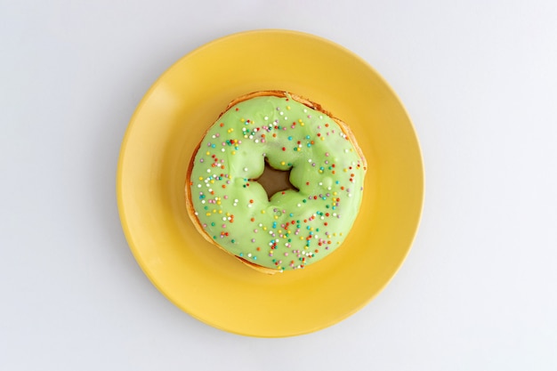 Einzelner grüner mattierter Donut in einer gelben Platte, Draufsicht.