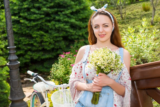 Einzelnes attraktives Mädchen, das lächelt und einen großen Strauß kleiner weißer Blumen hält, während es sich draußen auf das Geländer einer Brücke stützt