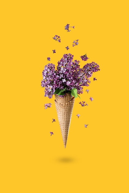 Eis aus lila Blüten im Waffelkegel auf gelbem Hintergrund von oben, schöne Blumenarrangements. Lila Blumen, die in Bewegung fallen oder fliegen. Muttertag, 8. März, Valentinstag, Geburtstag