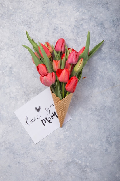 Eis der roten Tulpenblumen im Waffelkegel mit Karte Liebe Sie Mutter auf Betontischoberansicht im flachen Laienstil.