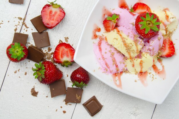 Eis mit Erdbeeren und Schokolade auf weißem Holztisch