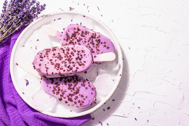 Eis mit violettem Lavendelgeschmack. Blumenstrauß, Vintage Silberlöffel, Keramikständer. Modernes hartes Licht, dunkler Schatten. Weißer Kitthintergrund, Draufsicht