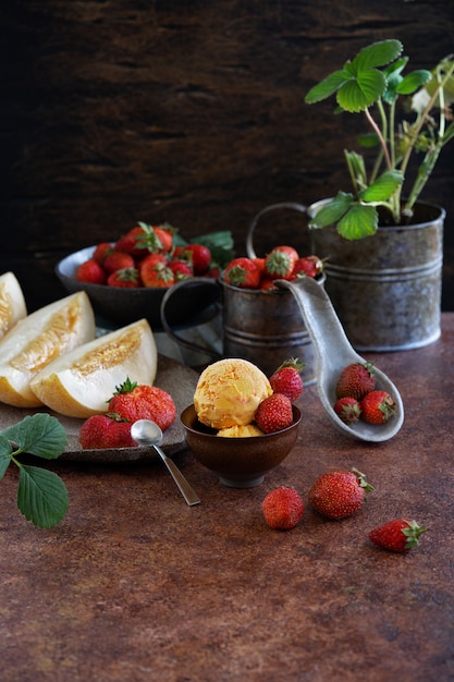 Eisbällchen mit Erdbeeren und Melonen in einer Keramikschale. Pflanzen Sie Erdbeeren in eine Vintage-Tasse