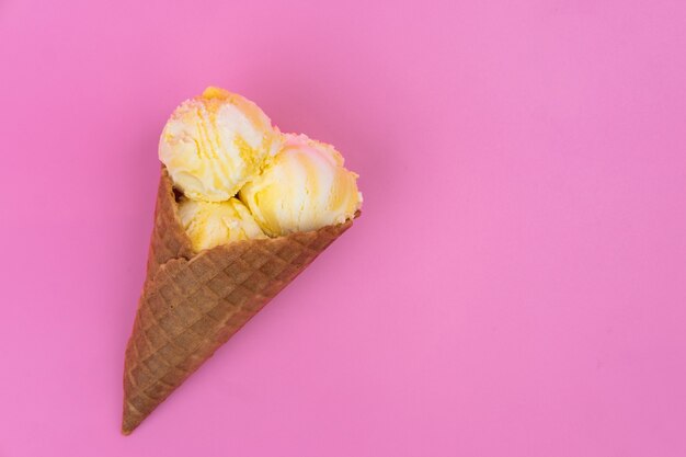 Eisbällchen mit Mangogeschmack in einer Waffeltüte auf rosa Hintergrund