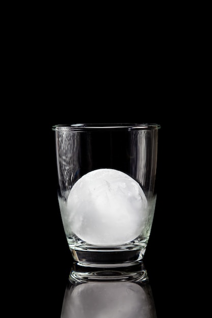 Eisball im Cocktailglas auf einem reflektierenden schwarzen Tisch.