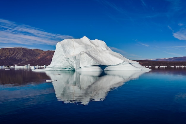 Eisberg im grönländischen Fjord mit Spiegelung im ruhigen Wasser. Sonniges Wetter. Goldene Stunde.