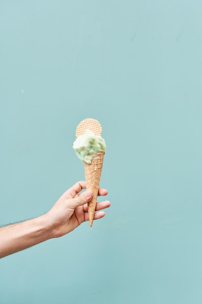 Eiscreme-Kegel auf blauem Hintergrund Mann, der das Eiscreme in der Hand hält