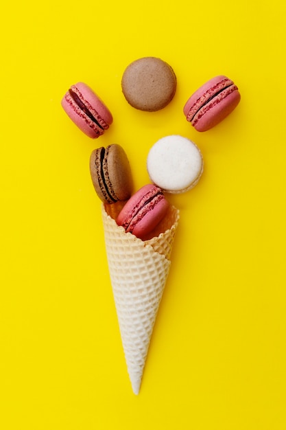 Eiscremewaffelkegel mit Makronen auf gelbem Hintergrund. Flach liegen, Dessert.