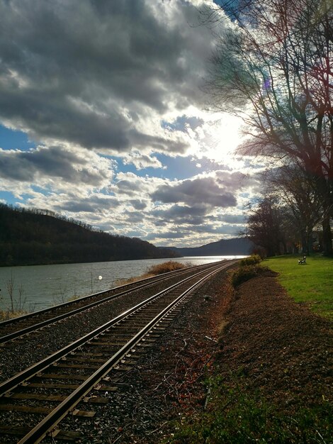 Eisenbahnschienen am Fluss gegen einen bewölkten Himmel