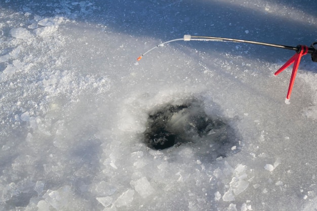 Eisfischen im Winter Eisfischen im Winter Kleine Angelrute steht in der Nähe eines Lochs im Eis eines Flusses