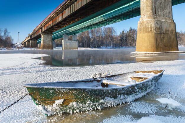 Eisiges Boot der frostigen Landschaft auf dem Hintergrund der Brücke über dem Fluss