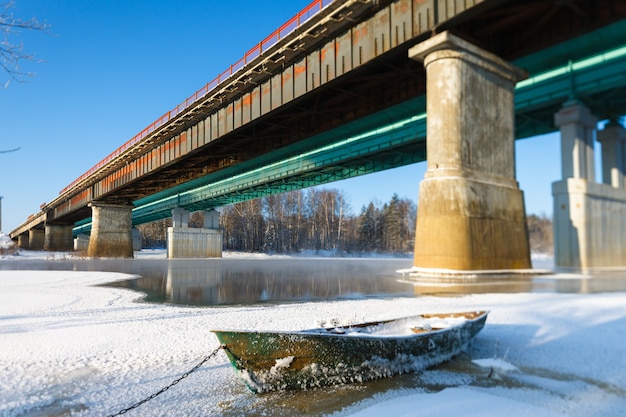 Eisiges Boot der frostigen Landschaft auf dem Hintergrund der Brücke über dem Fluss