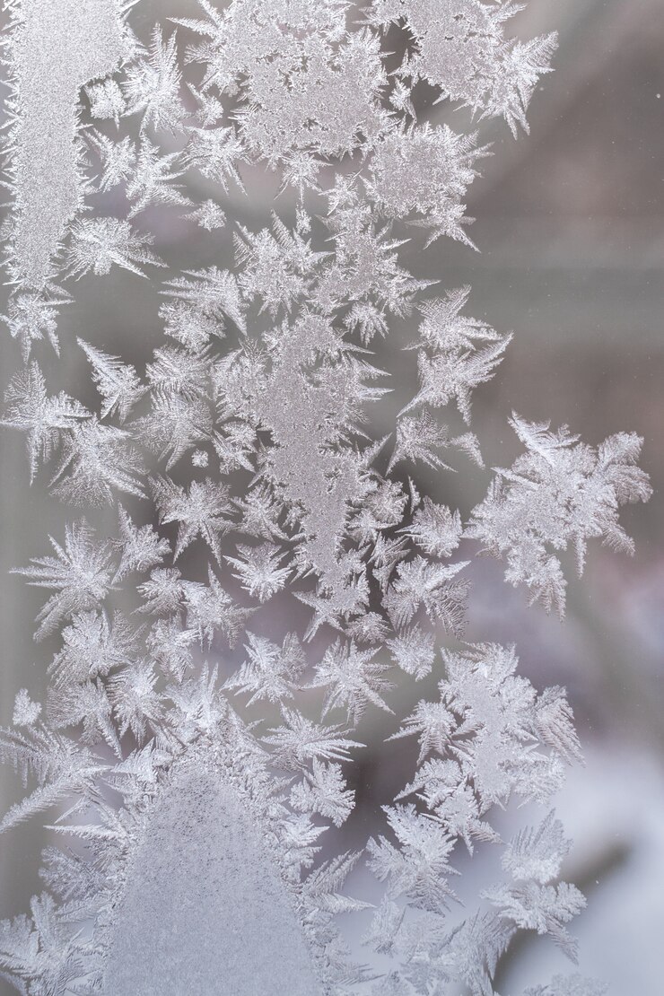 Eisiges Muster gemacht von den spitzen Schneeflocken auf Winterfensterglas.