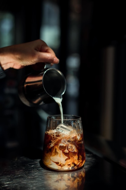 Eiskaffee auf einem Tisch mit Sahne, die hineingegossen wird und die Textur und das erfrischende Aussehen der