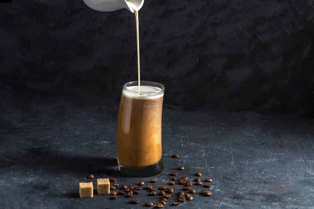 Eiskaffee Frappe in hohem Glas. Kühles Sommergetränk auf einem dunklen Hintergrund in zurückhaltendem. Milchstrom fließt in den Kaffee.