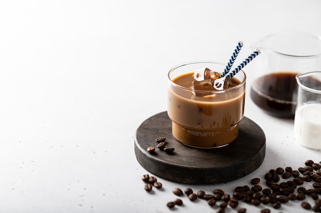 Eiskaffee mit Eiswürfeln in einem Glas auf einem Leuchttisch, Kaffeebohnen sind in der Nähe verstreut