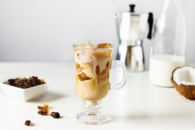 Eiskaffee mit Kokosmilch in einem hohen Glas auf weißem Holztisch