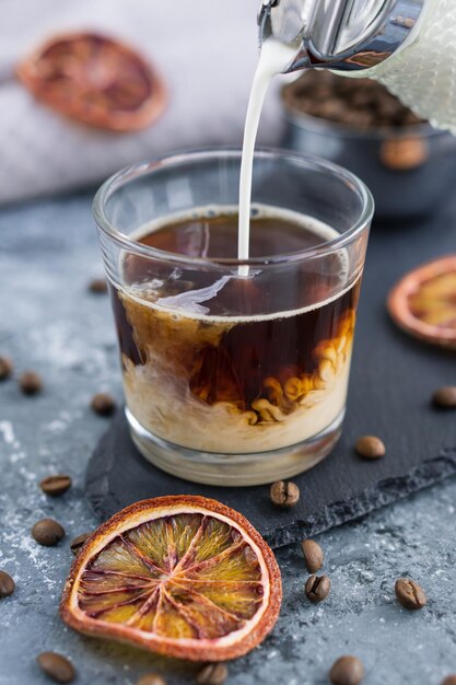 Eiskaffee mit Milch Sommergetränk Milch in Kaffee mit Eiswürfel auf grauem Hintergrund gießen