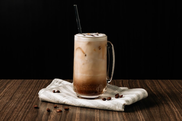 Eiskaffee mit Sahne in einem hohen Glas und Kaffeebohnen Portafilter Tamper und Milchkännchen auf dunklem Holzhintergrund Kaltes Sommergetränk