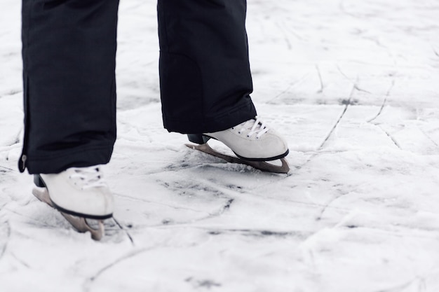 Eiskunstlauf-Schlittschuhe Nahaufnahme der Beine von man39 in schwarzen Winterhosen, die auf dem Eis des zugefrorenen Sees in weißen Eiskunstlauf-Schlittschuhen stehen
