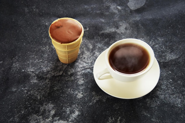 Eisschokolade in Waffeltasse mit weißem Keramikbecher heißem Tee auf dunklem Betonhintergrund