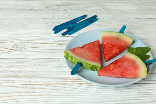 Eisstöcke mit Wassermelonenscheiben auf Teller auf weißem Holztisch