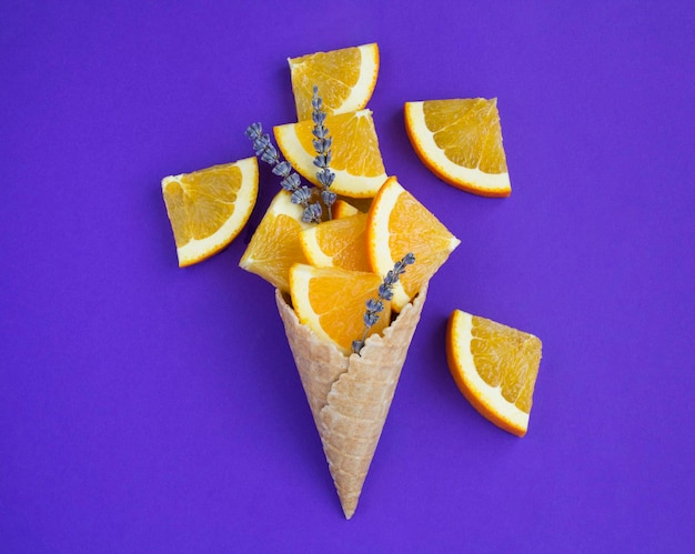 Eistüte mit gehackten orangefarbenen Früchten und Lavendelblüten auf violettem Hintergrund. Ansicht von oben. Platz kopieren.