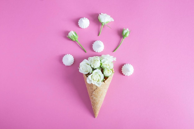 Eiswaffel mit weißen Rosen und Baiser auf rosa Hintergrund Draufsicht Nahaufnahme Kopierbereich