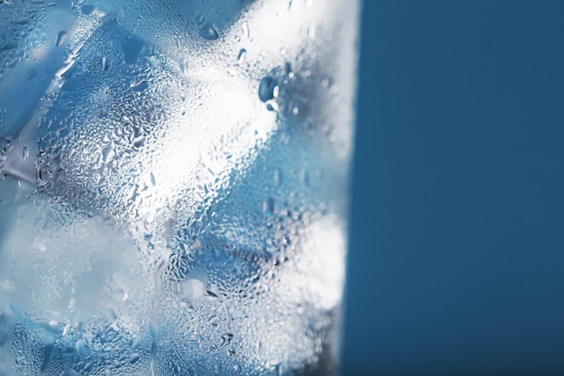 Eiswürfel in einem Glas mit erfrischendem Eiswasser auf blauem Grund.